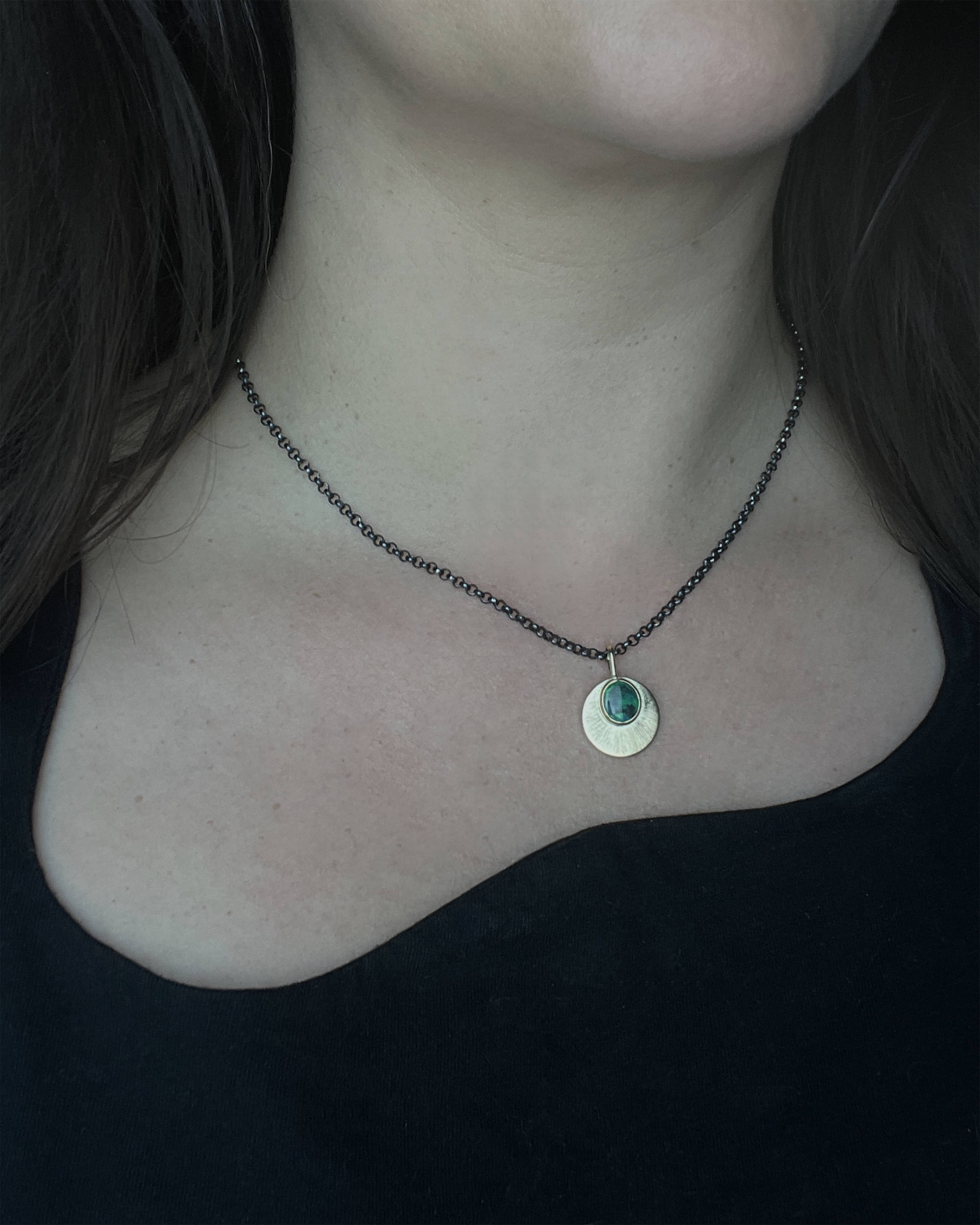 Australian Black Opal and 9ct Gold Pendant with engraved detail hangs from an oxidised sterling silver chain, and is worn by a person with an asymmetrical black top, worn on the shorter option on the chain.