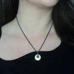 Australian Black Opal and 9ct Gold Pendant with engraved detail hangs from an oxidised sterling silver chain, and is worn by a person with an asymmetrical black top. 