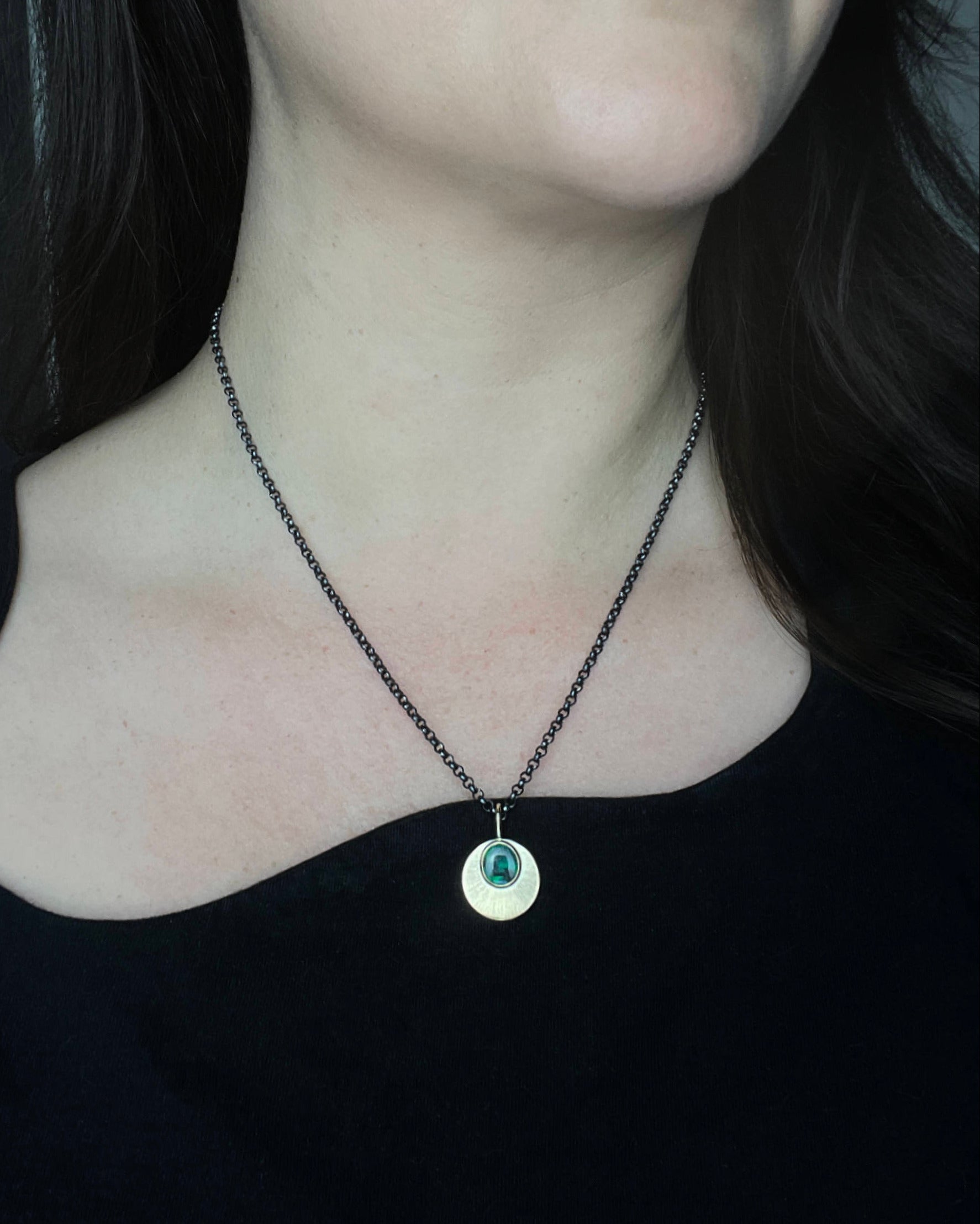 Australian Black Opal and 9ct Gold Pendant with engraved detail hangs from an oxidised sterling silver chain, and is worn by a person with an asymmetrical black top. 