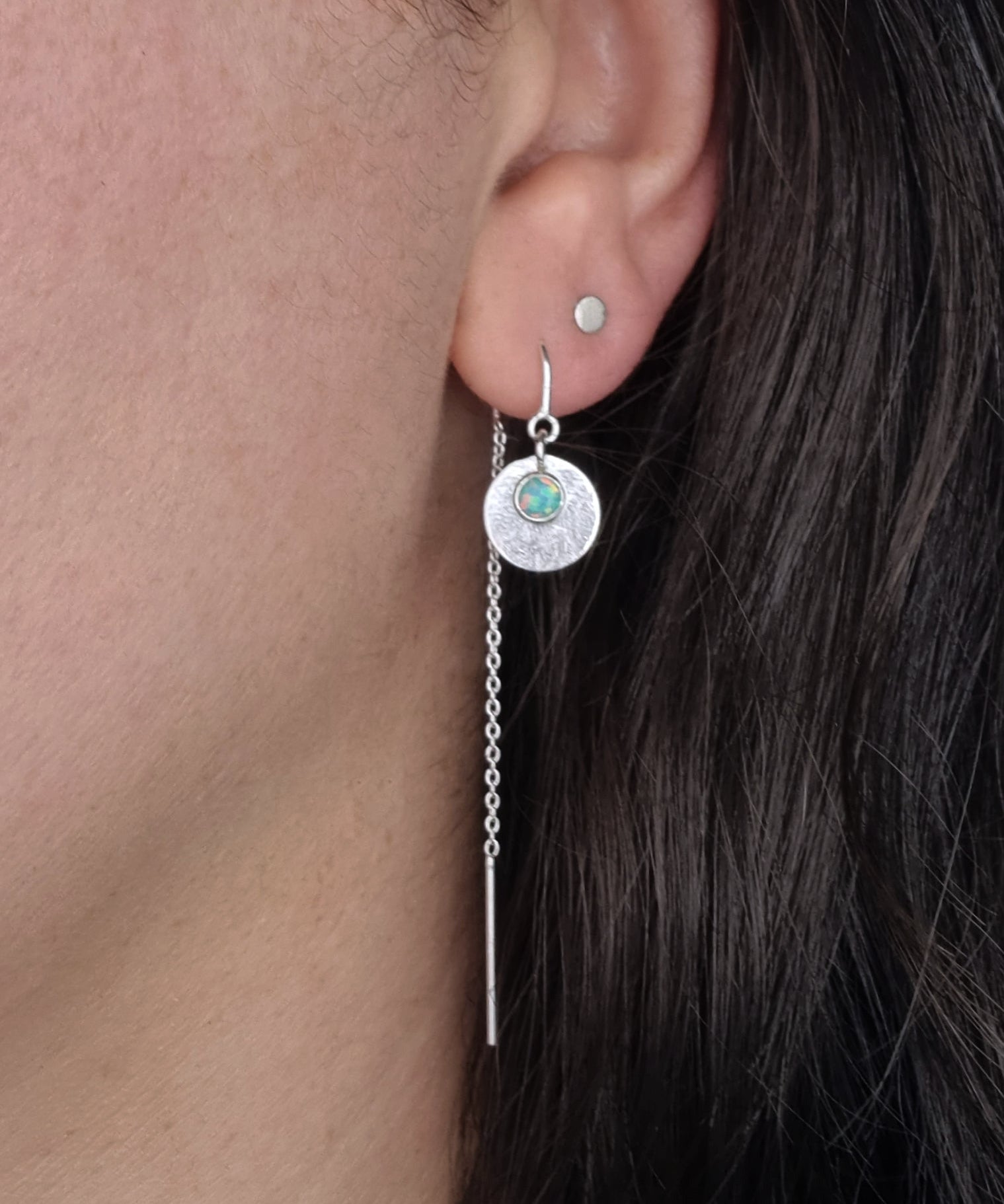 A Galaxy Opal Thread Earring, featuring a mint green gem, worn by a person with dark hair.