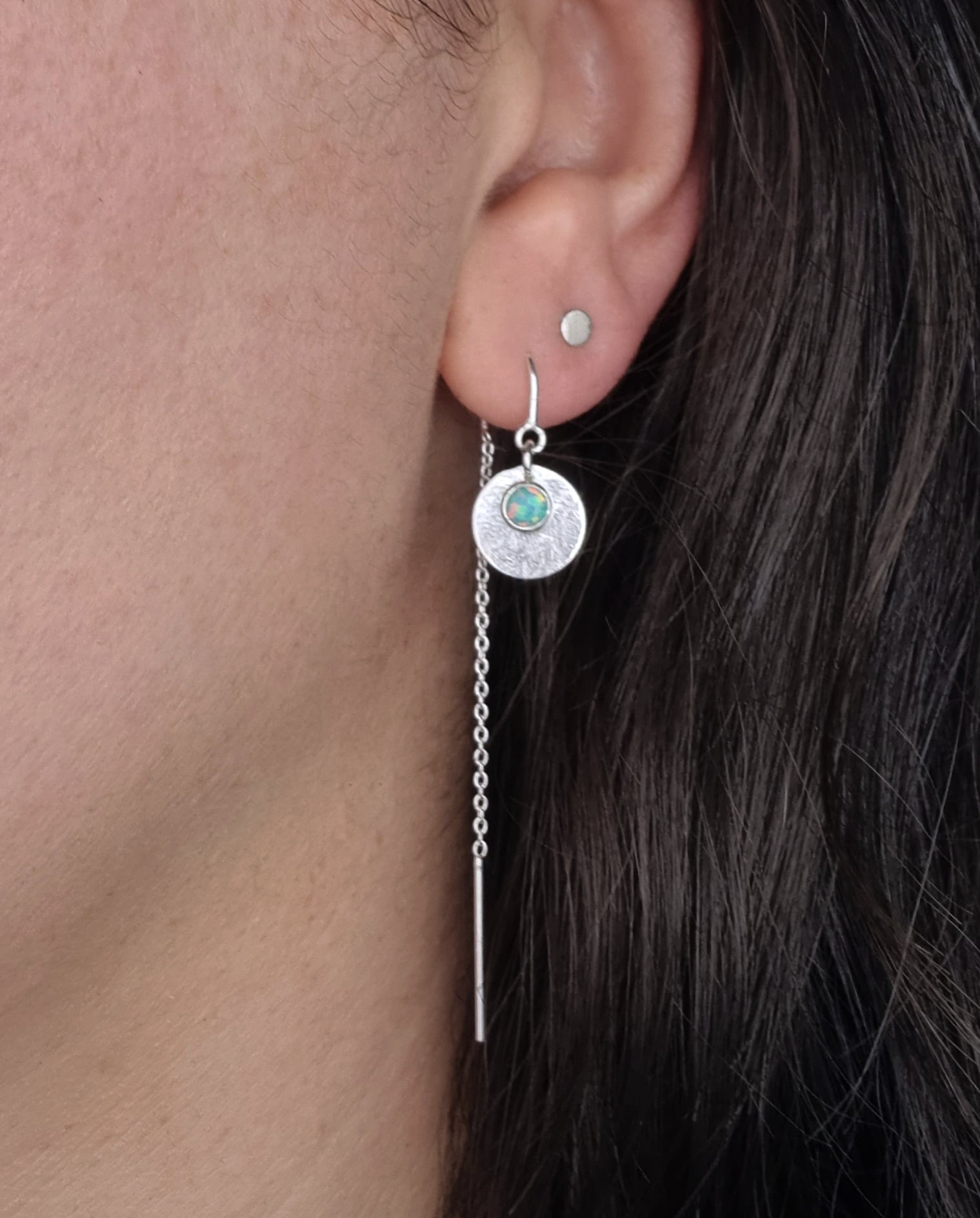 A Galaxy Opal Thread Earring, featuring a mint green gem, worn by a person with dark hair.
