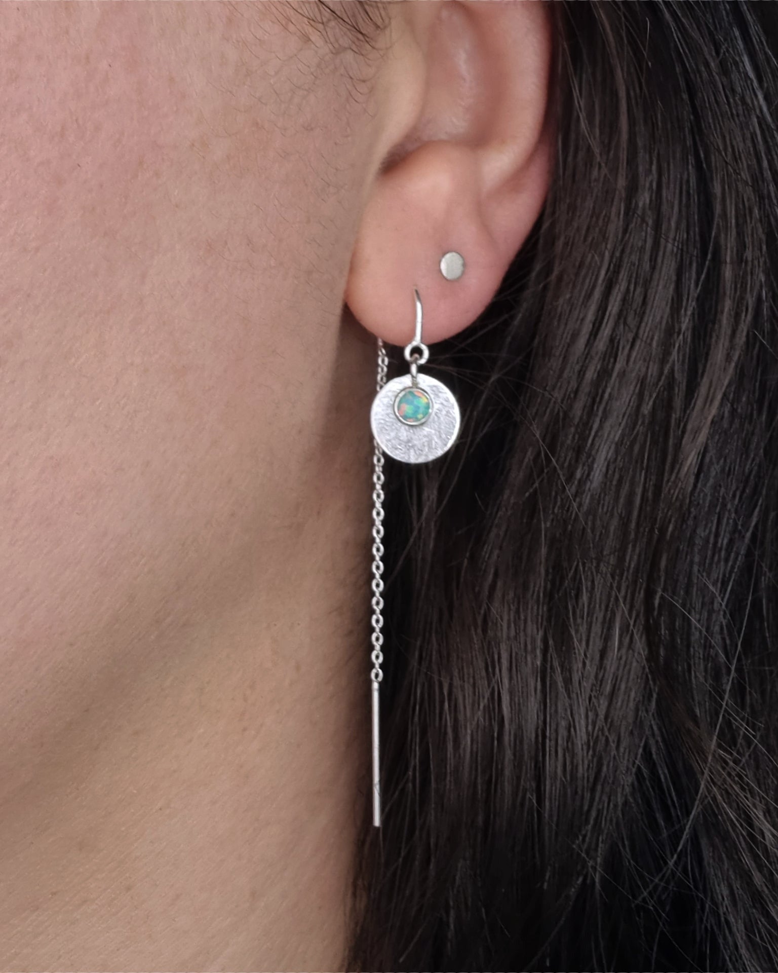 A Galaxy Opal Thread Earring, featuring a mint green gem, worn by a person with dark hair.