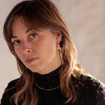 Woman with long brown hair wearing a black turtleneck, Gold Lunar Crescent Moon Thread Earrings, and a Pyrite Choker Necklace against a neutral background