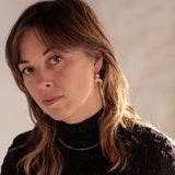 Woman with long brown hair wearing a black turtleneck, Gold Lunar Crescent Moon Thread Earrings, and a Pyrite Choker Necklace against a neutral background