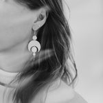 Close-up of a person wearing the Celestial Sterling Silver Earrings with a white background and light leaks across the photograph.