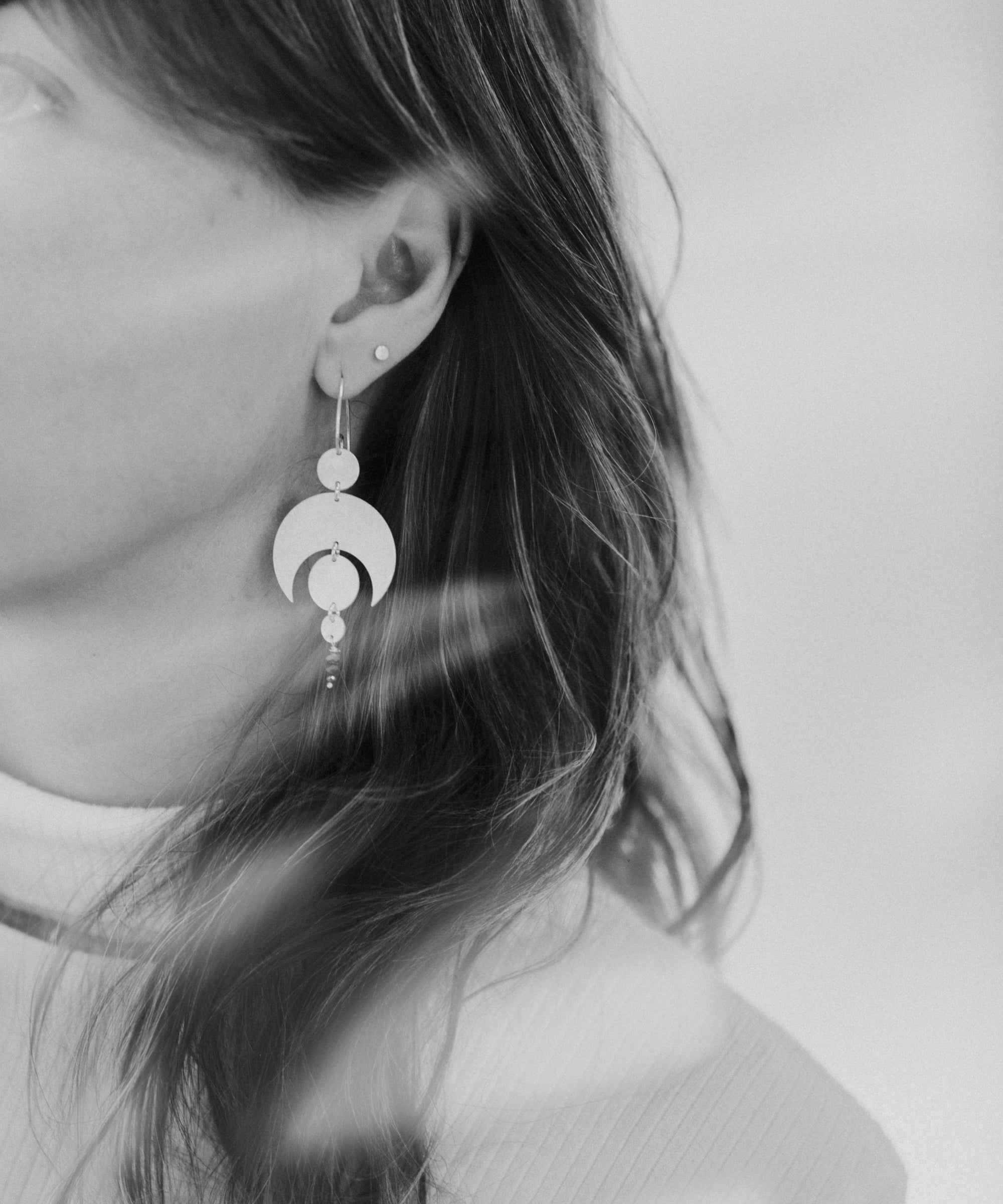 Close-up of a person wearing the Celestial Sterling Silver Earrings with a white background and light leaks across the photograph.