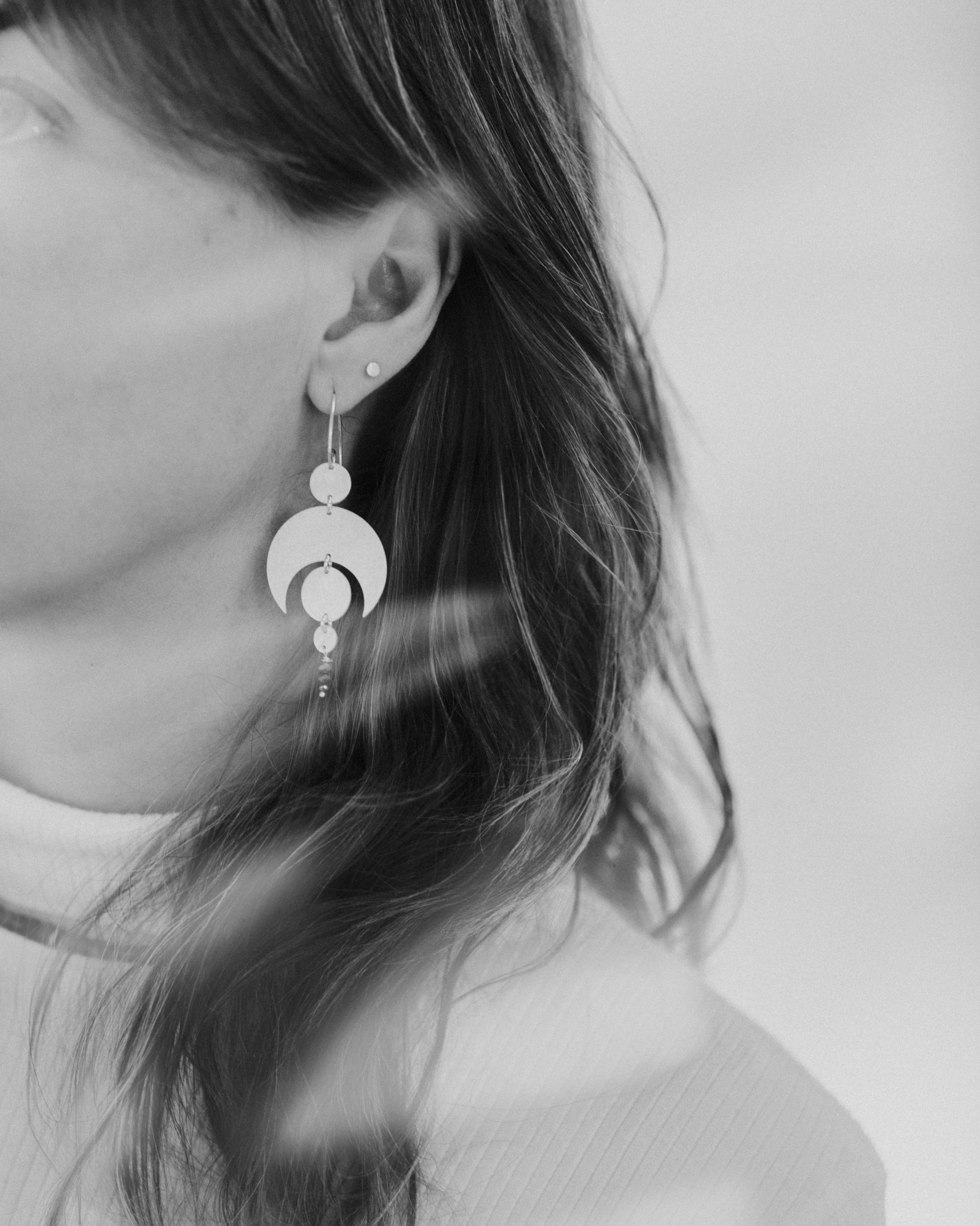 Close-up of a person wearing the Celestial Sterling Silver Earrings with a white background and light leaks across the photograph.