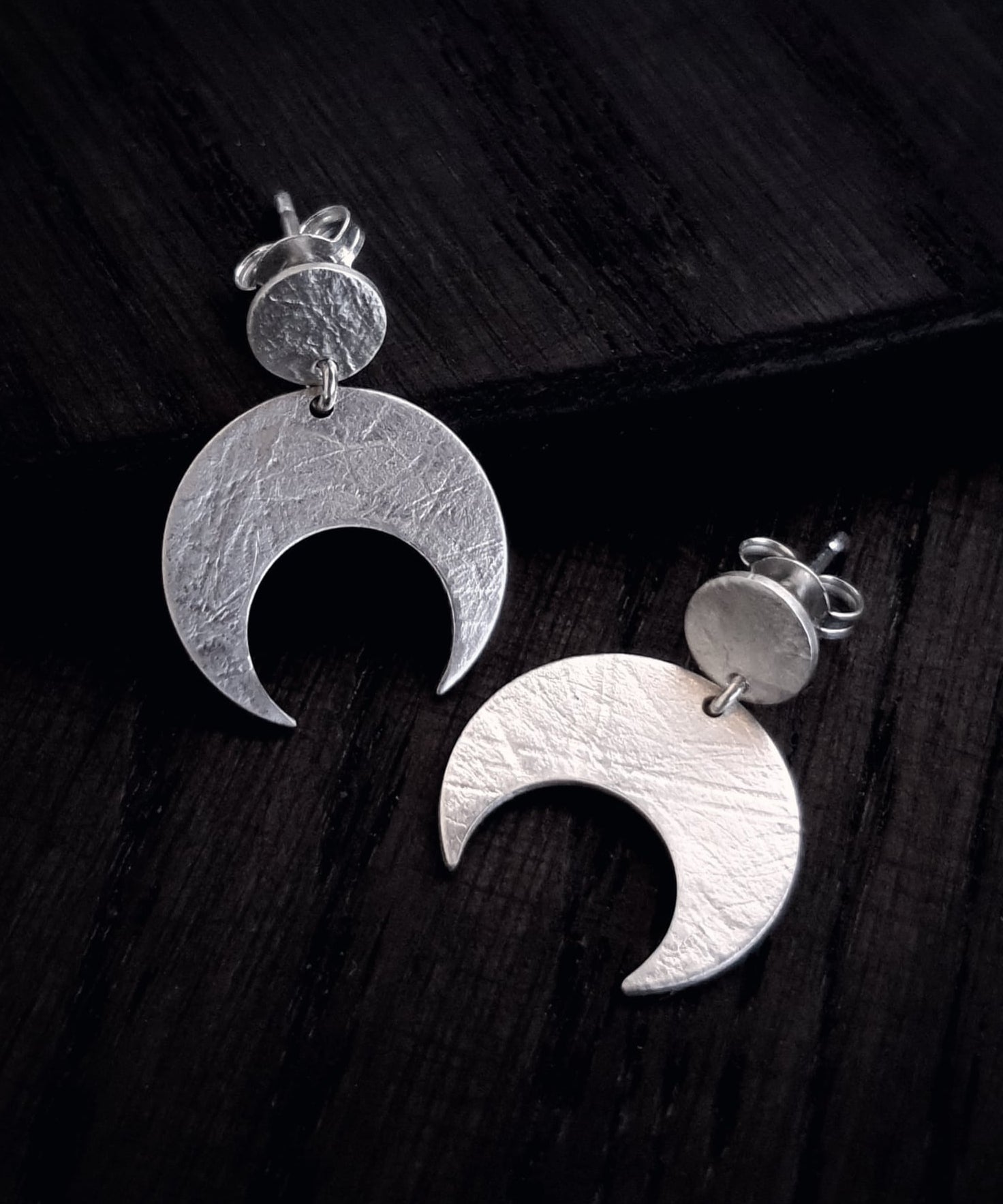 Sterling Silver Lunar crescent moon earrings on a dark wooden surface.