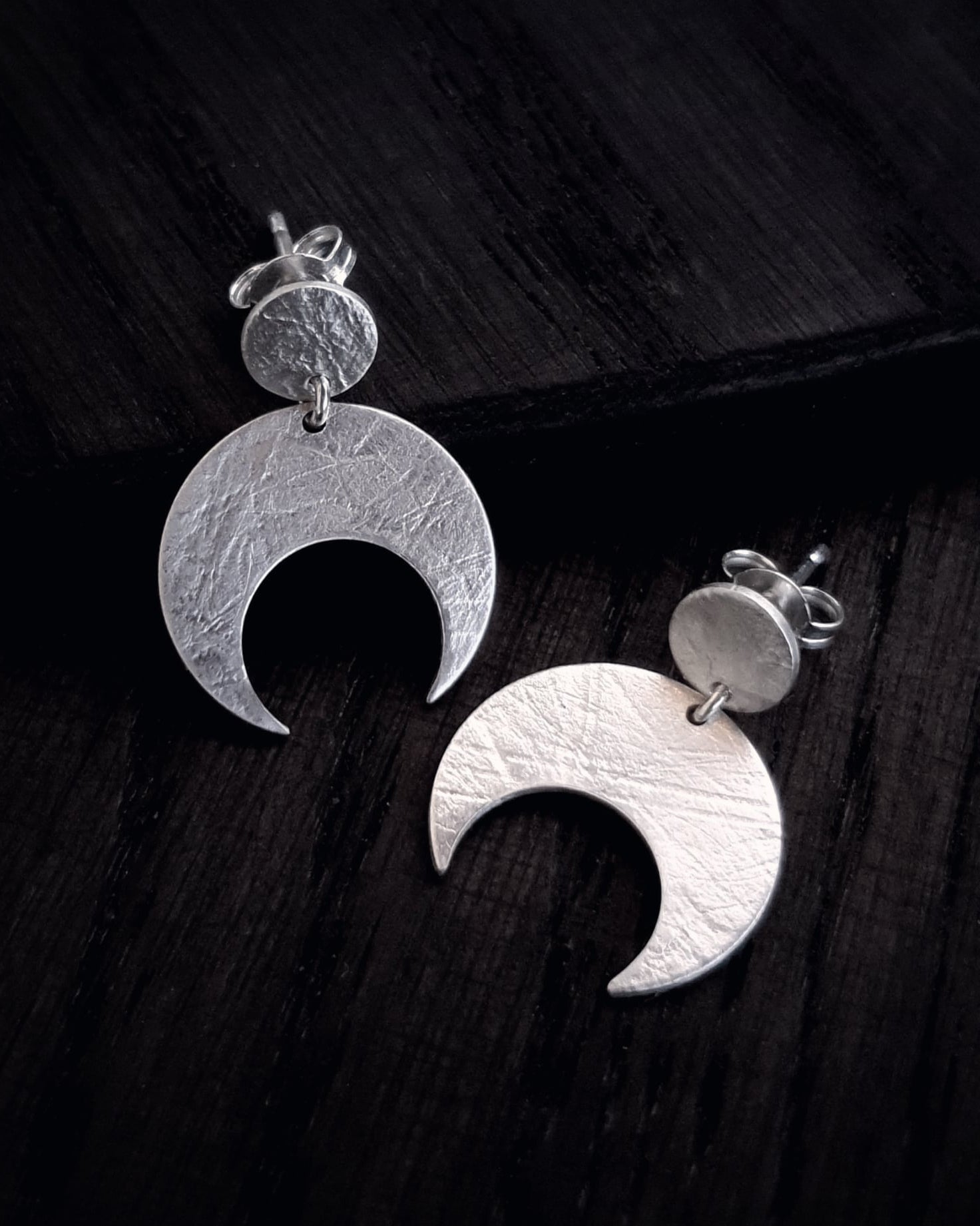 Sterling Silver Lunar crescent moon earrings on a dark wooden surface.