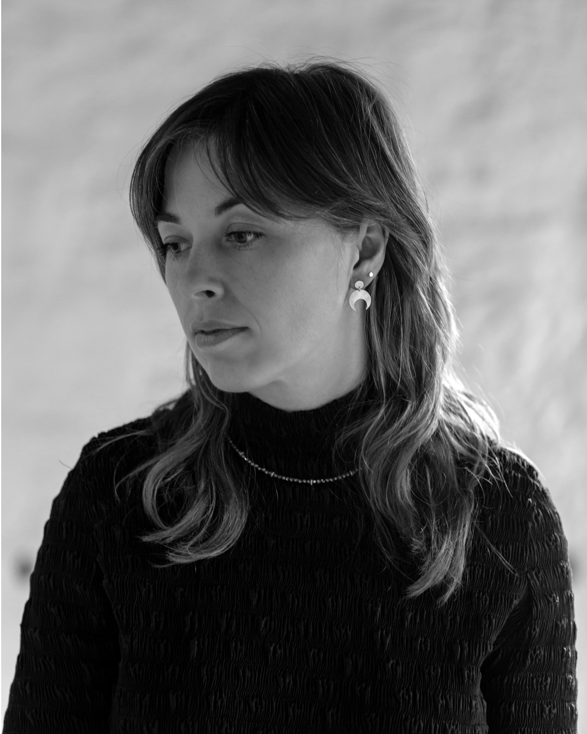 Black and white portrait of a woman with long hair wearing the Lunar Stud earrings and Pyrite Choker necklace.