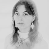 Black and white portrait of a person with long hair. They are wearing the Celestial Earrings, which feature a crescent moon and circles representing planetary alignment. They also wear large quartz rings.