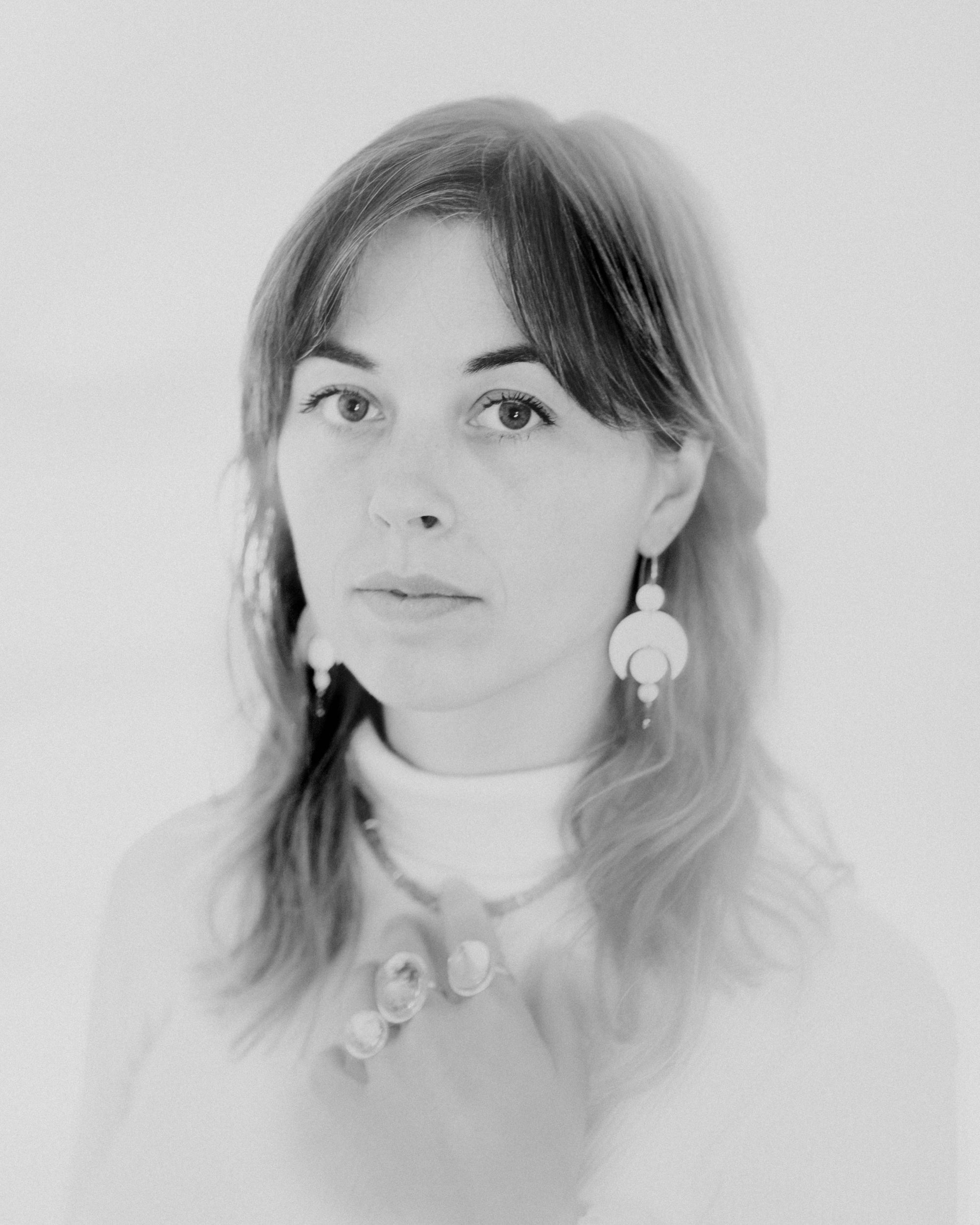 Black and white portrait of a person with long hair. They are wearing the Celestial Earrings, which feature a crescent moon and circles representing planetary alignment. They also wear large quartz rings.
