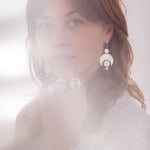 A soft photograph with light leaks of a person with long hair wearing the Celestial Crescent Moon earrings.
