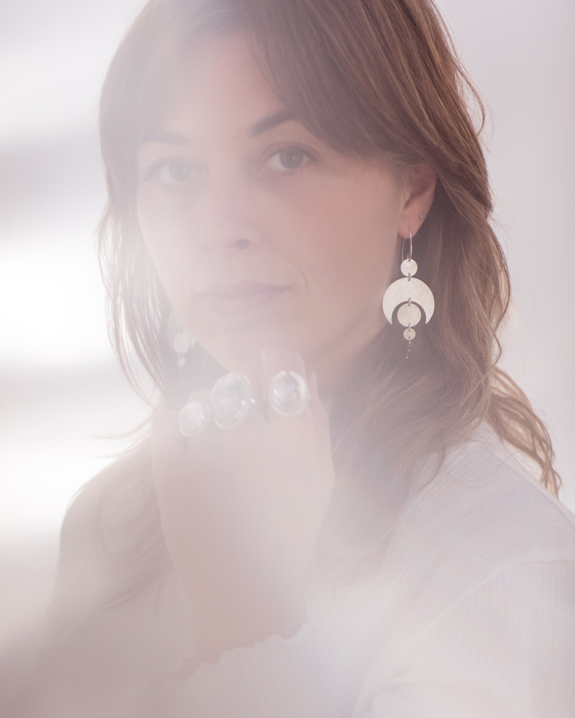 A soft photograph with light leaks of a person with long hair wearing the Celestial Crescent Moon earrings.