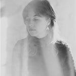 Black and white portrait of a person with shoulder-length hair against a light background. They are wearing the Lunar Thread Earrings. These sterling silver earrings feature a textured disc and crescent moon hanging from a hook and fine chain fitting.