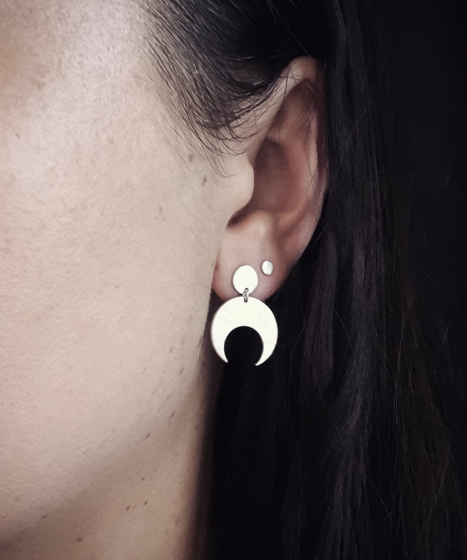 Close-up of an ear wearing the Sterling Silver Lunar stud earrings with a dark background. These earrings feature a textured crescent moon design. 