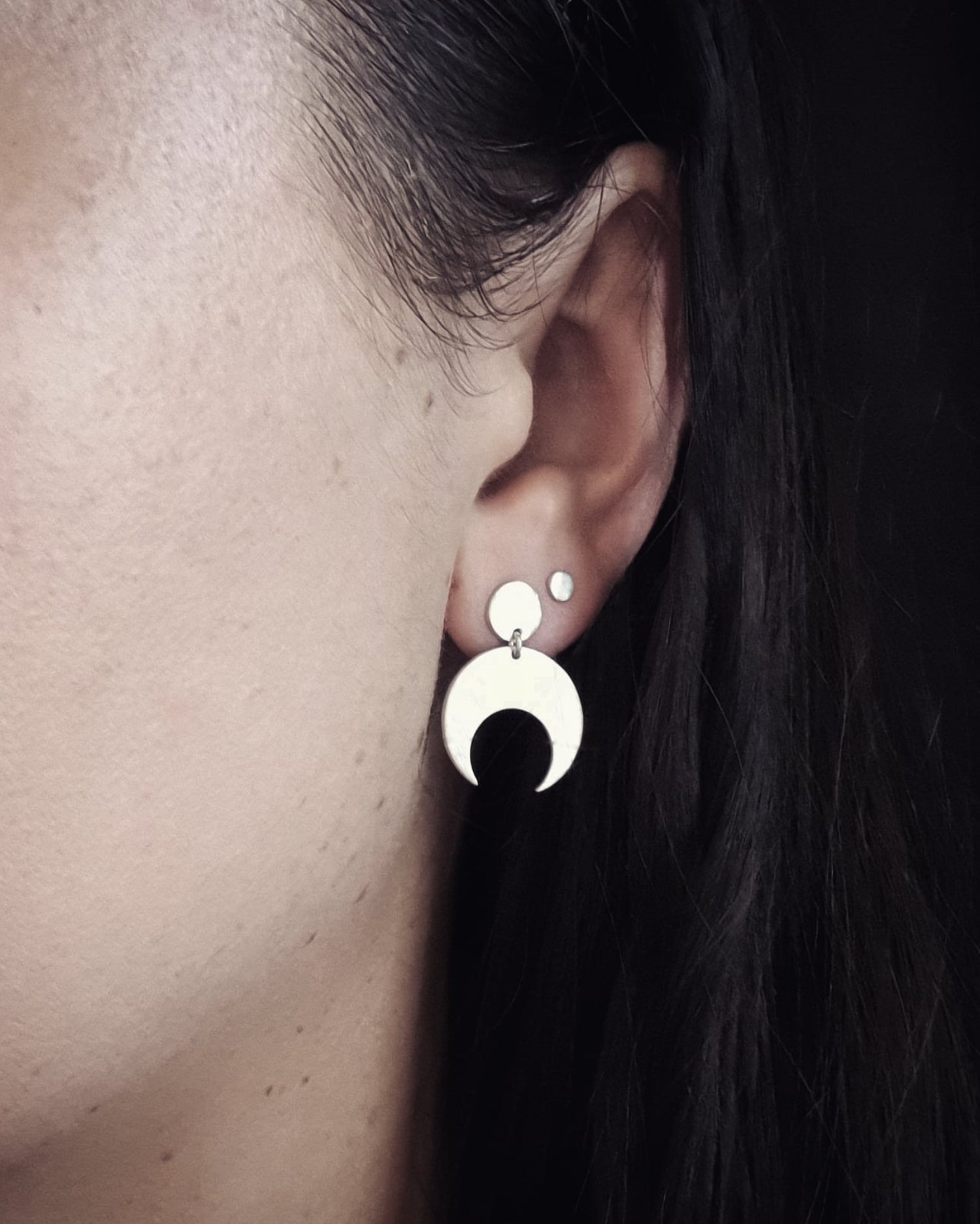 Close-up of an ear wearing the Sterling Silver Lunar stud earrings with a dark background. These earrings feature a textured crescent moon design. 