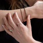 Close-up of a person's wrist and hand wearing Pyrite and gold bracelets, an Australian Gold Opal Ring, and the Trinity mixed metals rings.