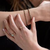 Close-up of a person's wrist and hand wearing Pyrite and gold bracelets, an Australian Gold Opal Ring, and the Trinity mixed metals rings.