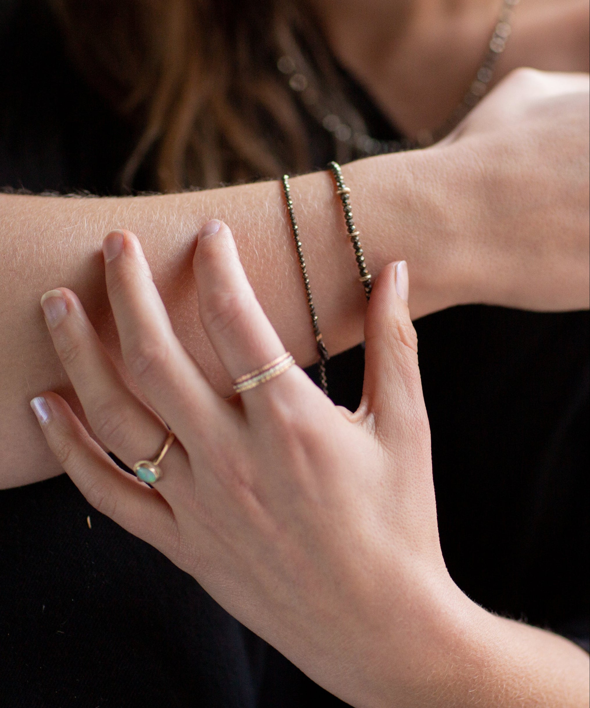 Close-up of a person's wrist and hand wearing Pyrite and gold bracelets, an Australian Gold Opal Ring, and the Trinity mixed metals rings.