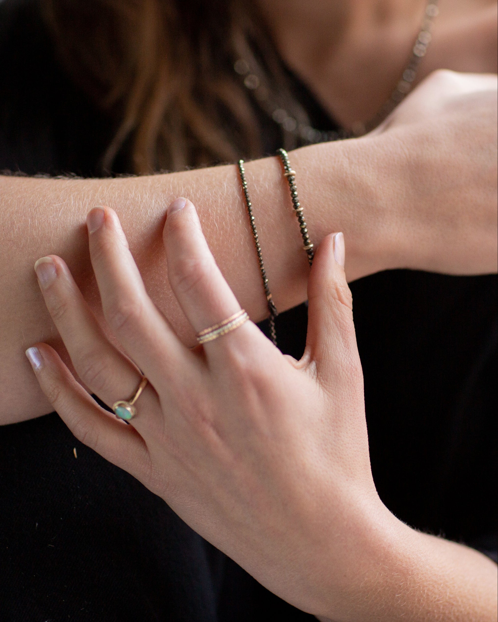 Close-up of a person's wrist and hand wearing Pyrite and gold bracelets, an Australian Gold Opal Ring, and the Trinity mixed metals rings.