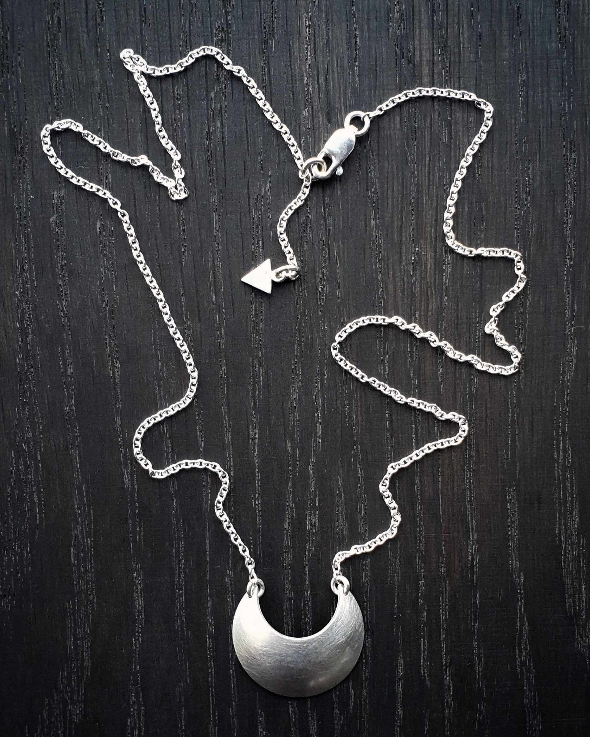 Sterling Silver Luna Crescens necklace featuring a crescent moon on a dark wooden surface
