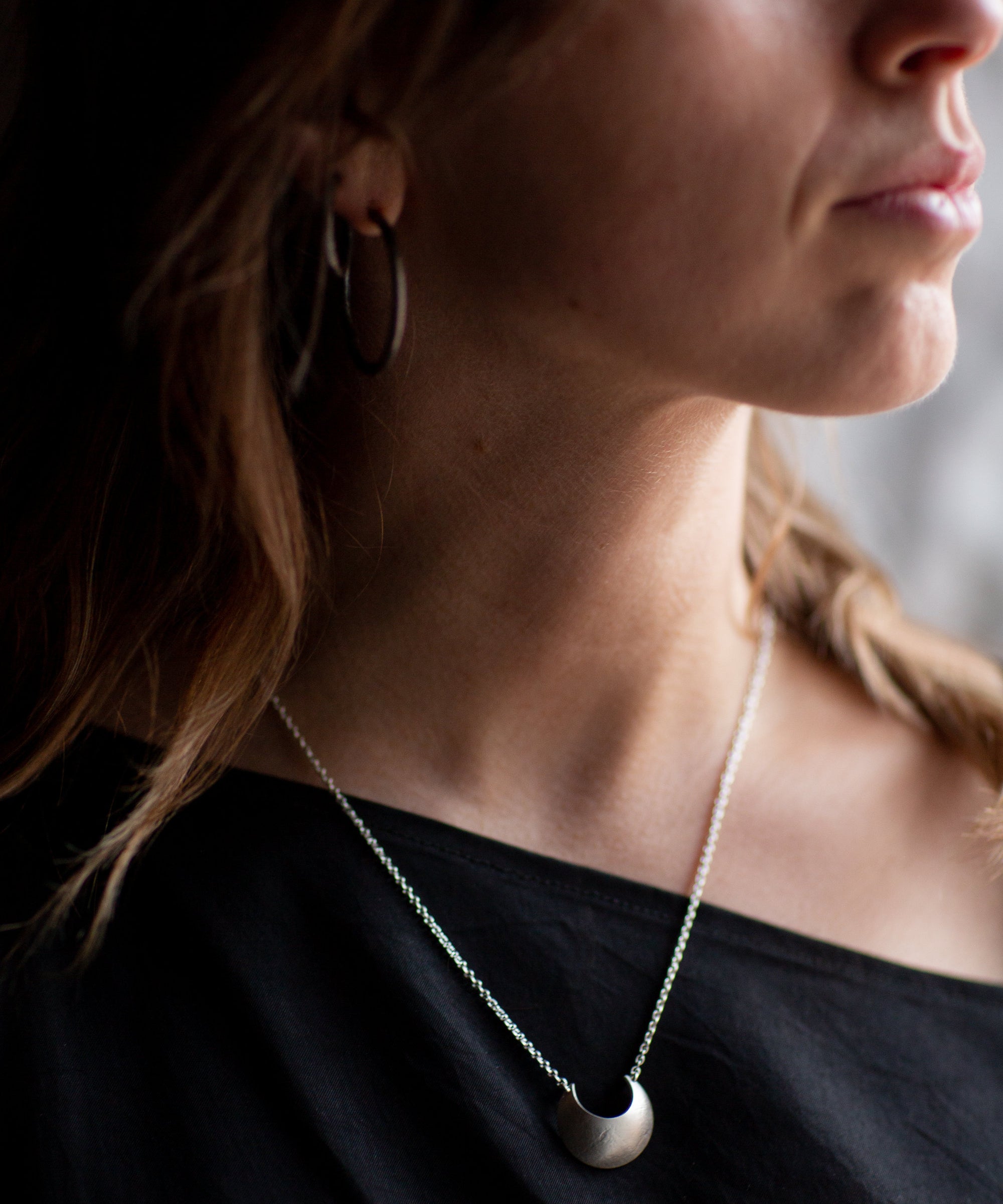 Close-up of a person wearing a Sterling Silver Luna Crescens necklace featuring a crescent moon by Emily Eliza Arlotte