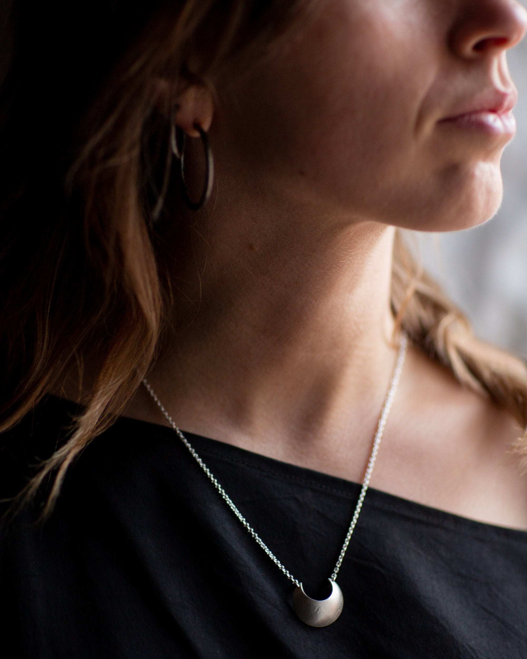 Close-up of a person wearing a Sterling Silver Luna Crescens necklace featuring a crescent moon by Emily Eliza Arlotte