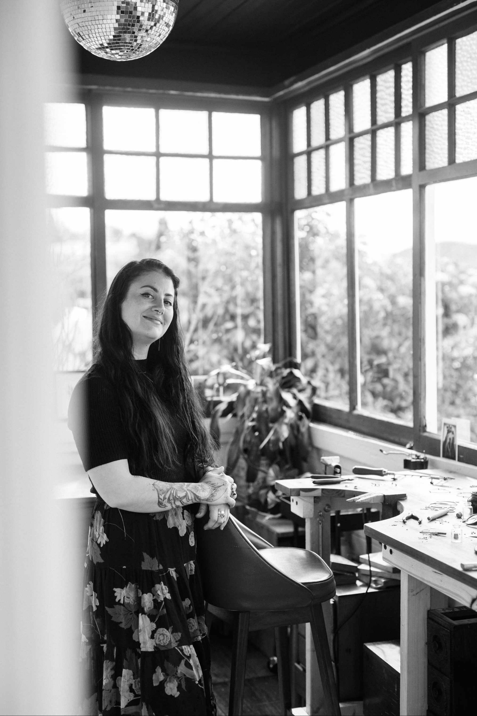 Emily Eliza Arlotte standing in their jewellery studio in Hobart, with large windows, looking out onto trees.