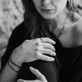 Black and white photo of a woman holding her knee with a blurred background. She is wearing Pyrite and Gold Bracelets, and mixed metal rings.