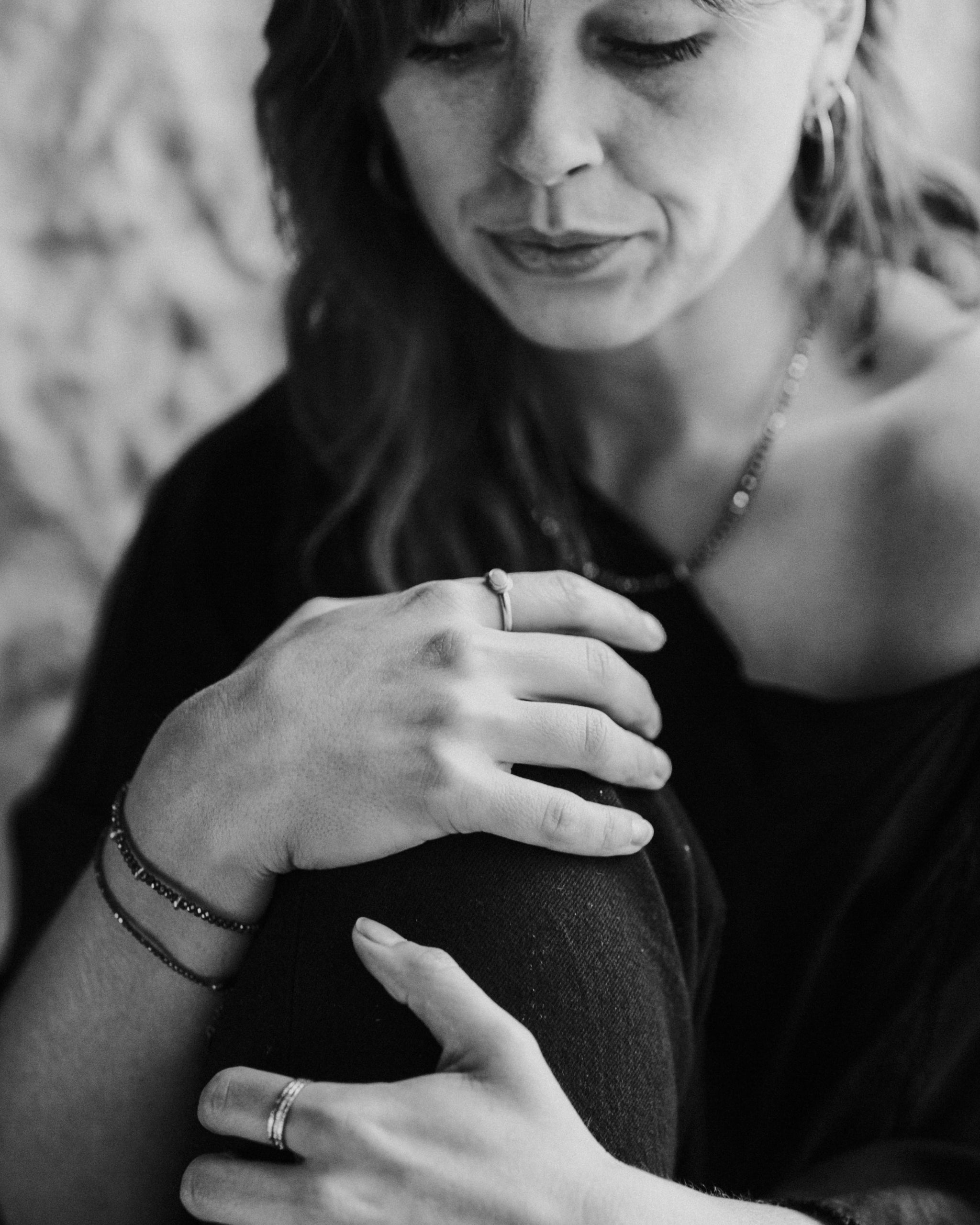 Black and white photo of a woman holding her knee with a blurred background. She is wearing Pyrite and Gold Bracelets, and mixed metal rings.