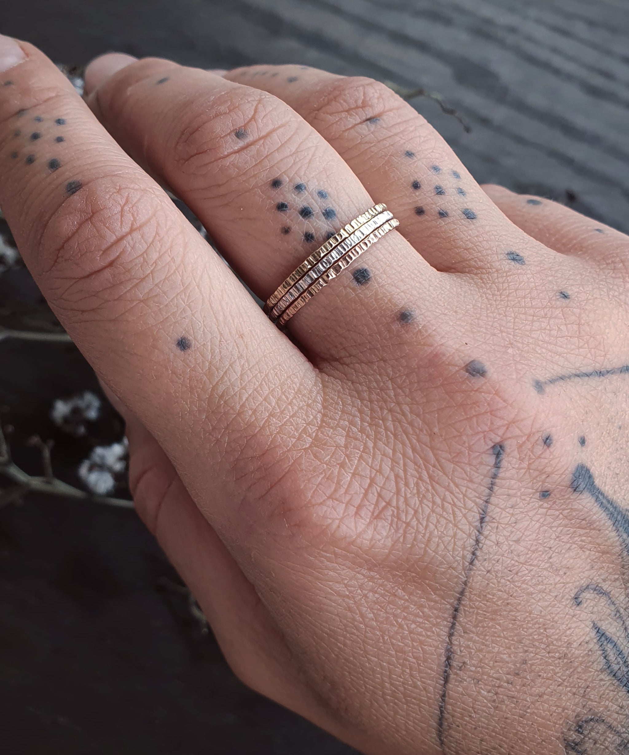 A tattooed hand wearing the Yellow Gold, Rose Gold, and Sterling Silver Stack Rings.