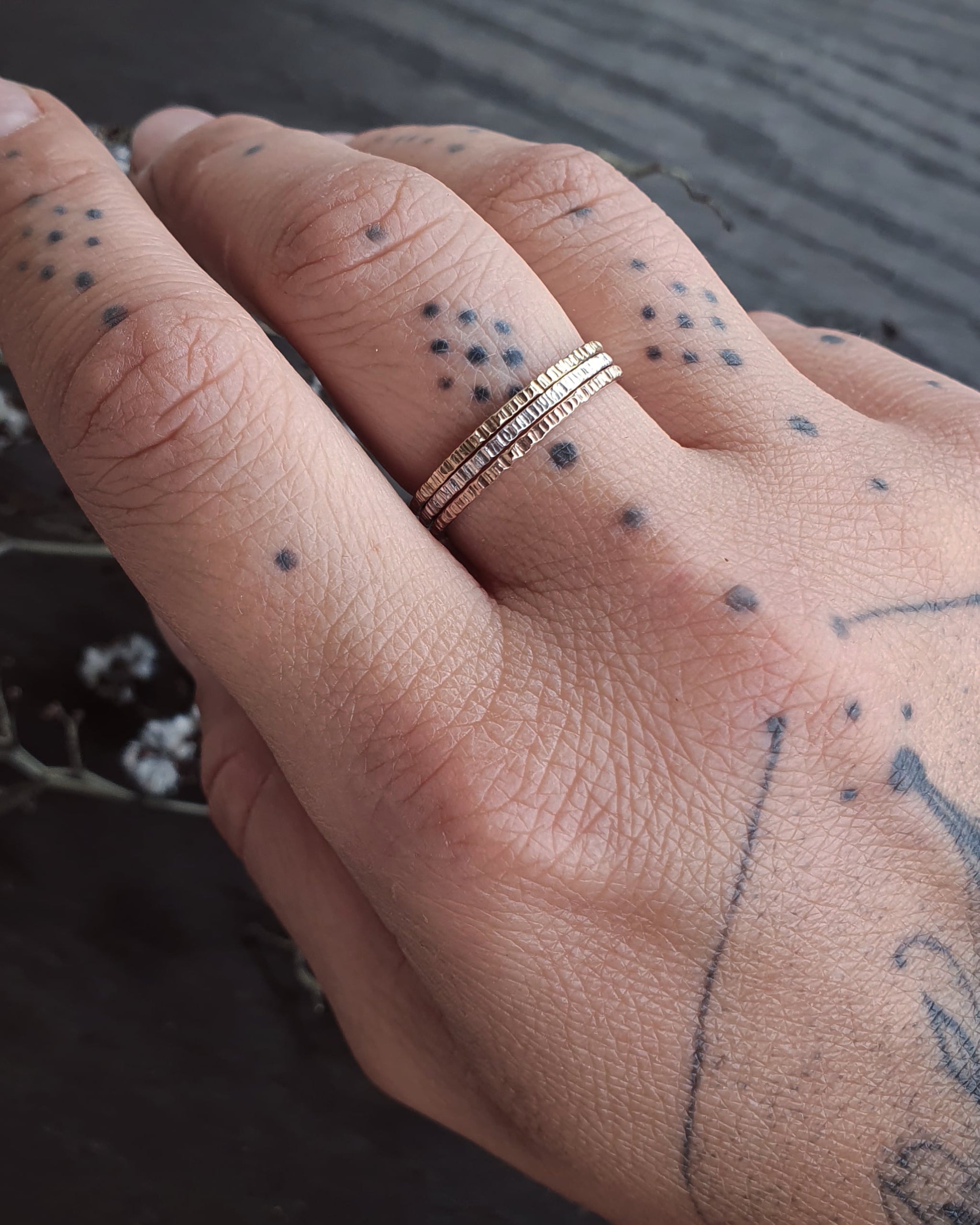 A tattooed hand wearing the Yellow Gold, Rose Gold, and Sterling Silver Stack Rings.