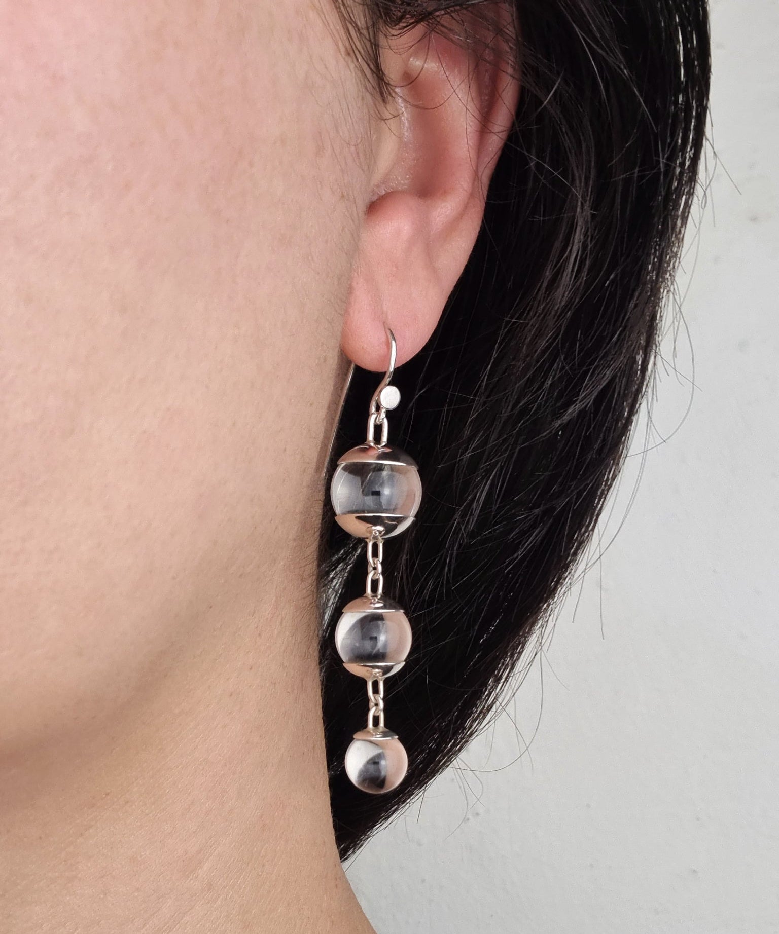 A pair of sterling silver drop earrings featuring three quartz spheres attached to small silver hooks, worn by a person with dark hair.