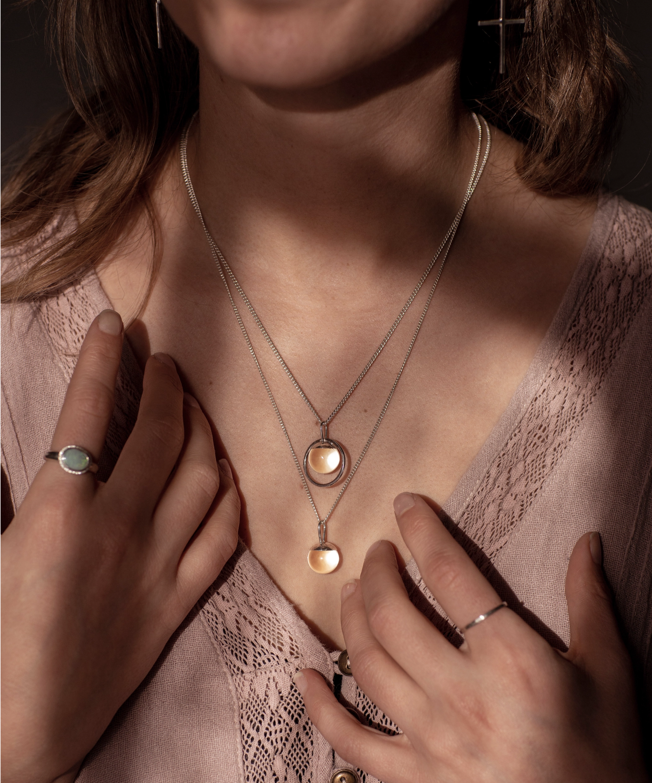 The Divination Necklace, which featuring a glowing quartz sphere on each pendant, are worn by a person wearing pink with dappled light landing on them.