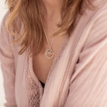 A person in a pink linen shirt is wearing the Divination Necklace by Emily Eliza Arlotte. Photography by Cassie Sullivan.