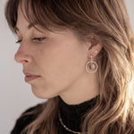 A person with a sweeping wolf-cut hairdo looking to the left wearing the Divination Stud Earrings, handmade by Emily Eliza Arlotte in Hobart, Tasmania. The earrings featuring a clear quartz crystal ball inside a hoop and hung from a stud fitting.