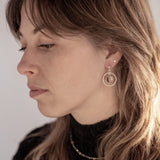 A person with a sweeping wolf-cut hairdo looking to the left wearing the Divination Stud Earrings, handmade by Emily Eliza Arlotte in Hobart, Tasmania. The earrings featuring a clear quartz crystal ball inside a hoop and hung from a stud fitting.