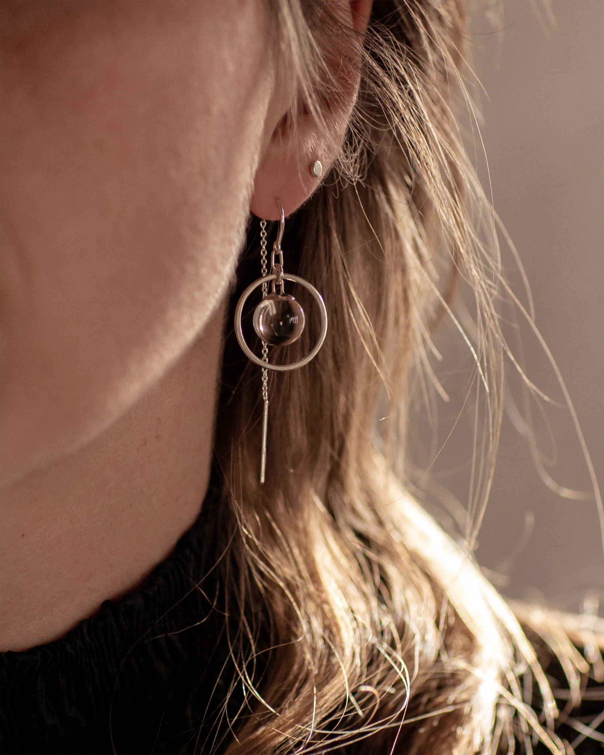 Close-up of a person wearing the Sterling Silver Divination Quartz Sphere Threader Earrings with a blurred background.
