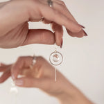 Close-up of a hands holding the Divination Thread Earrings with another hand out of focus in the background holding the Lunar Thread Earrings.