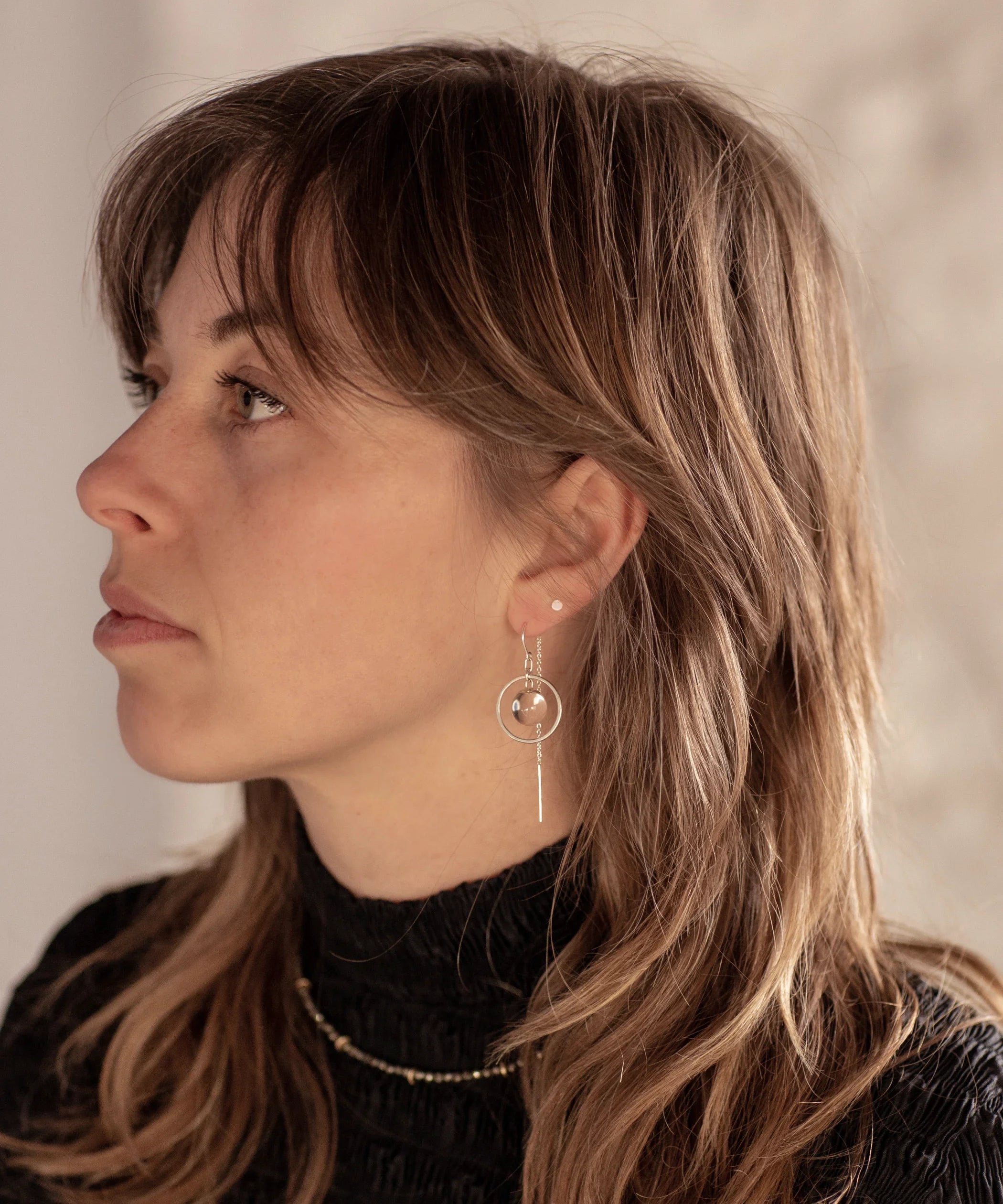 A person with brown wolf-cut hair wearing the Divination Thread Earrings and the Pyrite Choker Necklace
