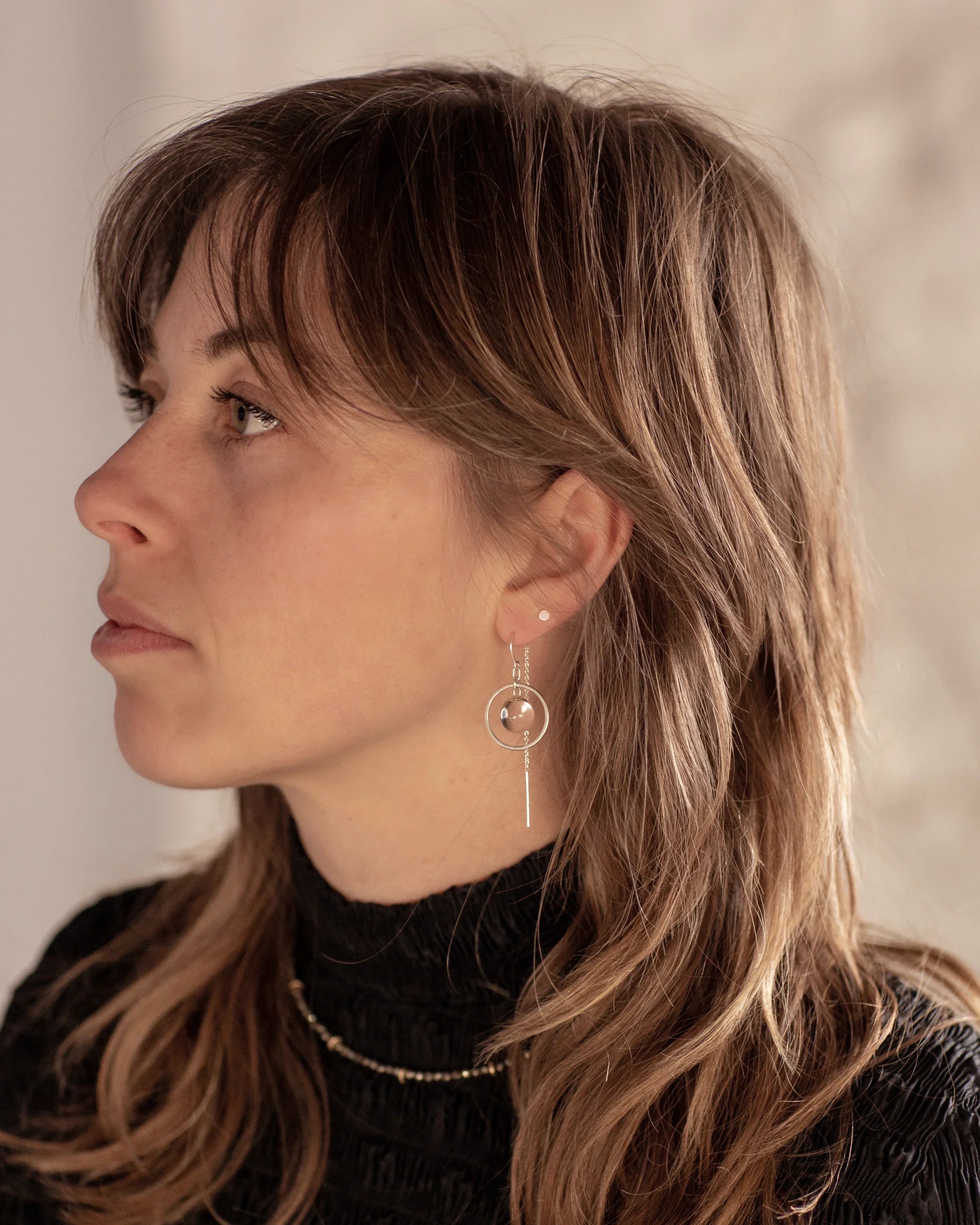 A person with brown wolf-cut hair wearing the Divination Thread Earrings and the Pyrite Choker Necklace