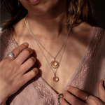 The Divination Necklaces, which feature a glowing quartz orb on each pendant, are worn by a person wearing pink with dappled light landing on them.