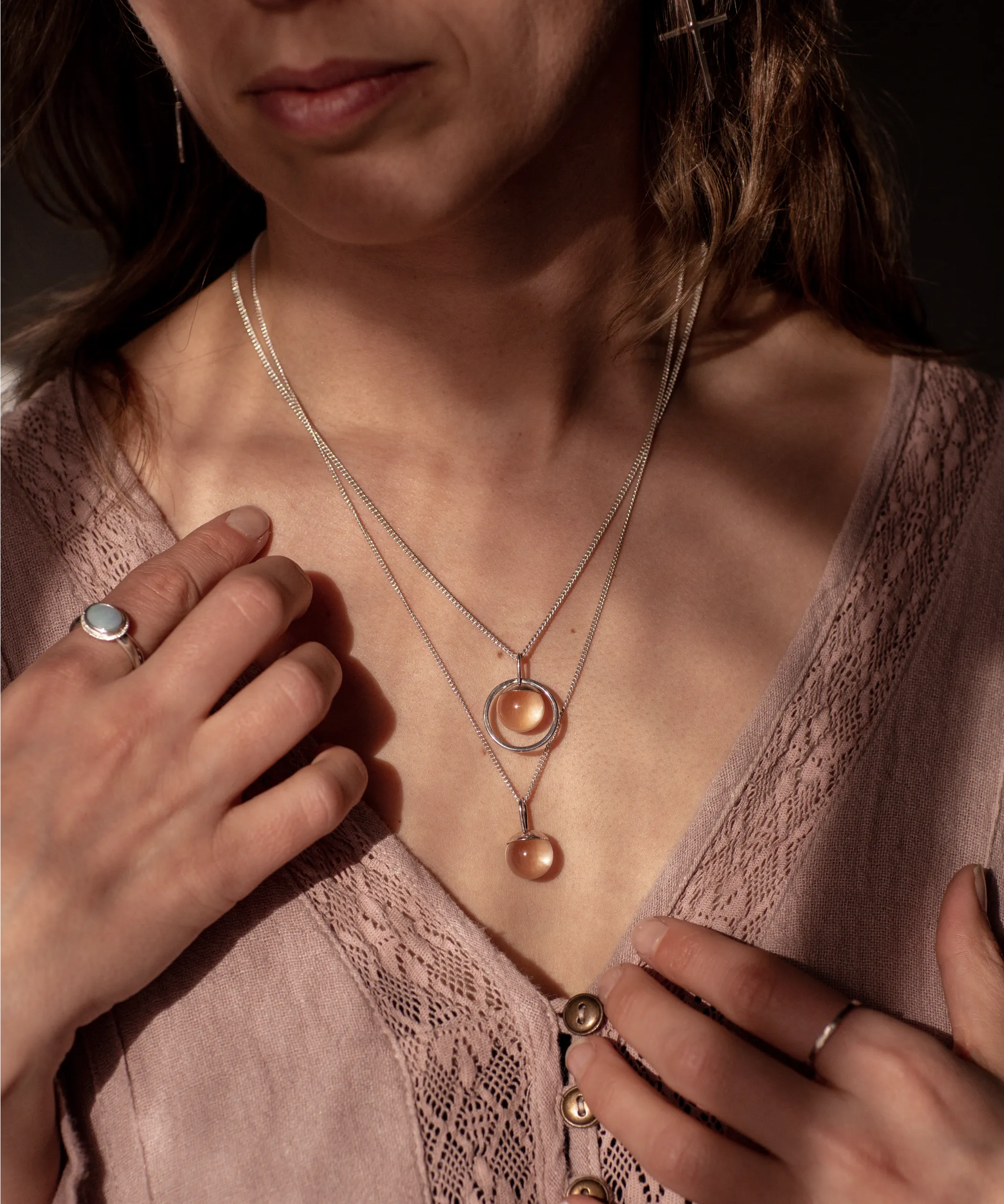 The Divination Necklaces, which feature a glowing quartz orb on each pendant, are worn by a person wearing pink with dappled light landing on them.