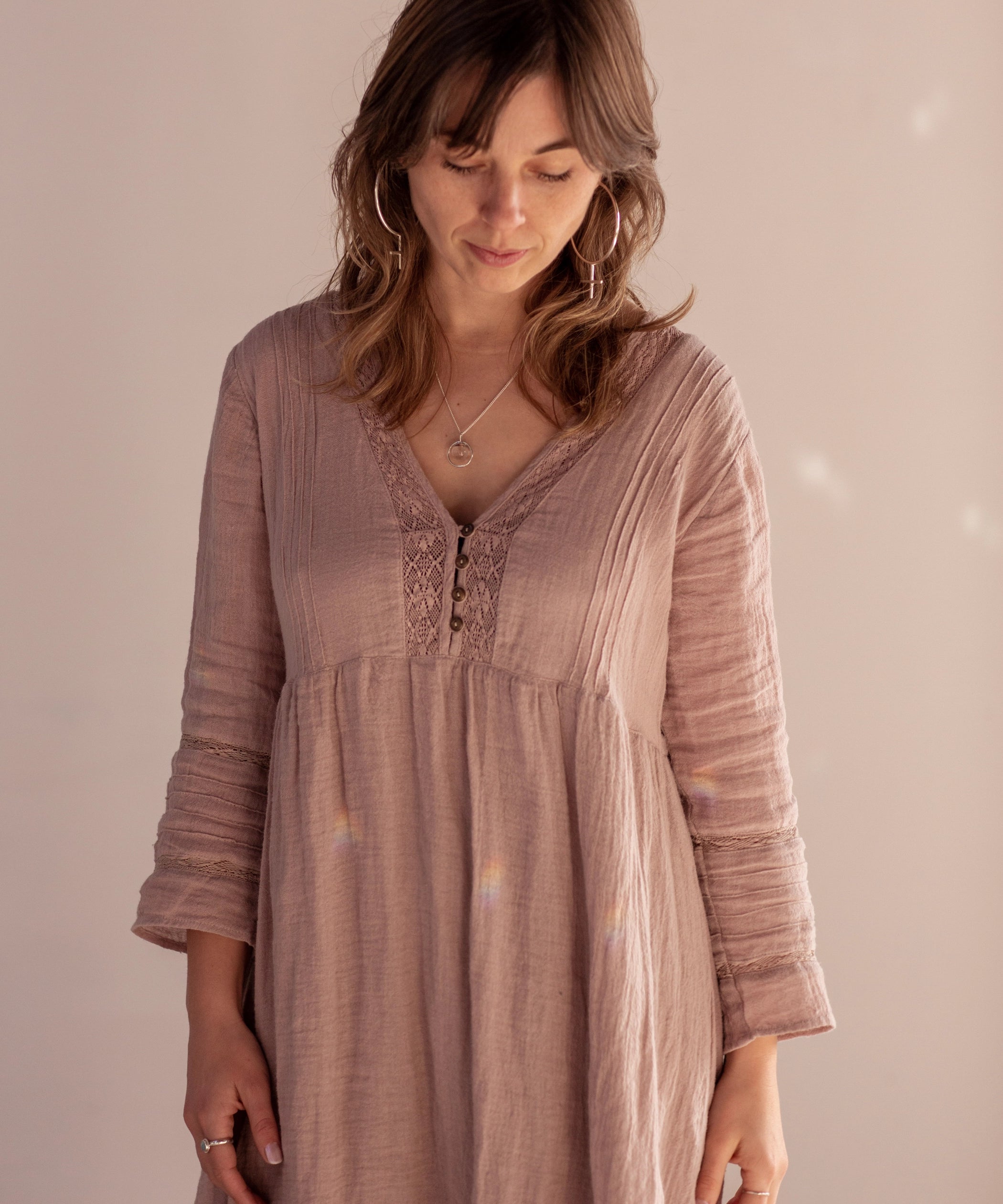 A person wearing a linen pink dress stands facing downwards, wearing the Venus Hoop Earrings and Divination Necklace, both handmade in Hobart Tasmania by Emily Eliza Arlotte.