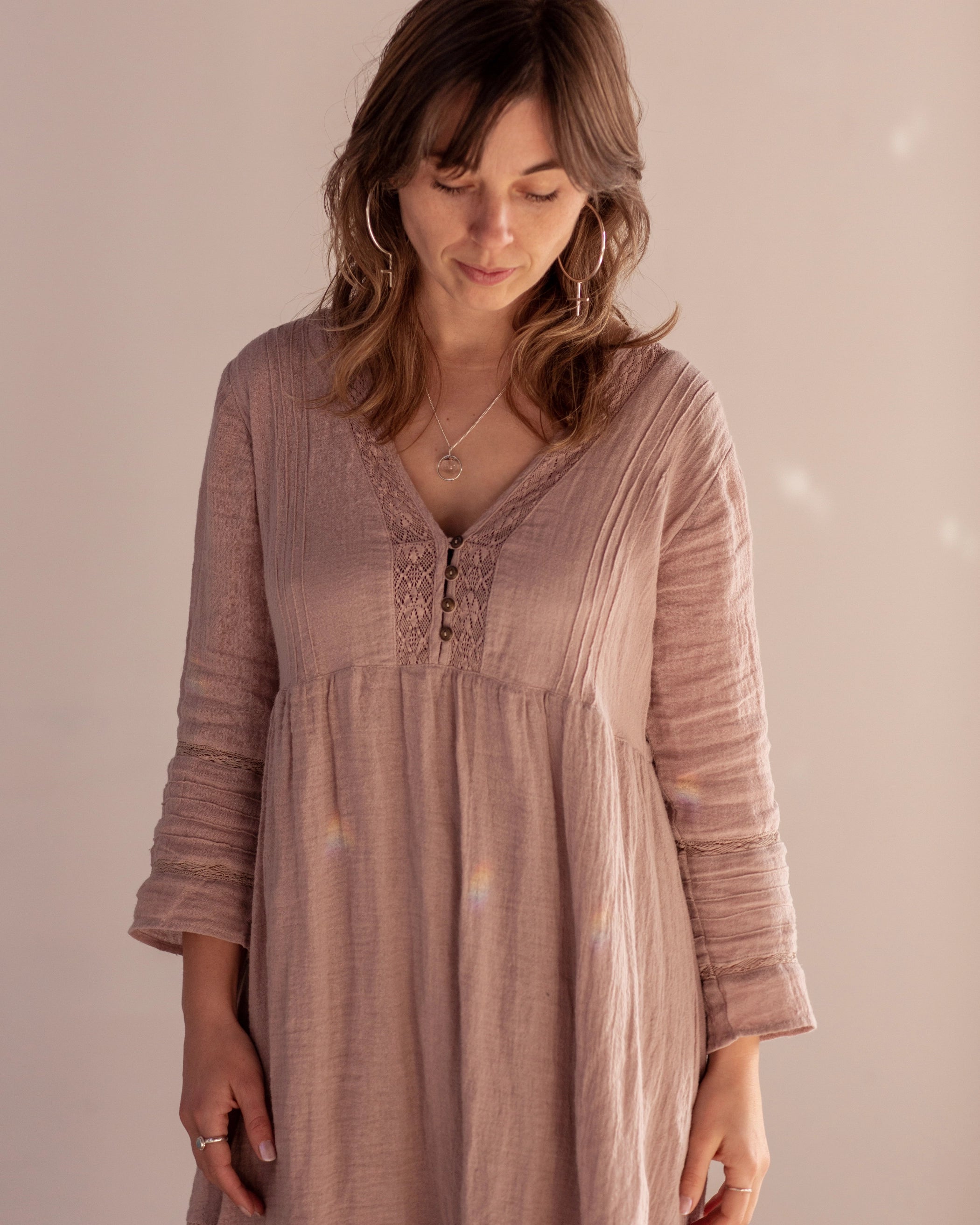 A person wearing a linen pink dress stands facing downwards, wearing the Venus Hoop Earrings and Divination Necklace, both handmade in Hobart Tasmania by Emily Eliza Arlotte.