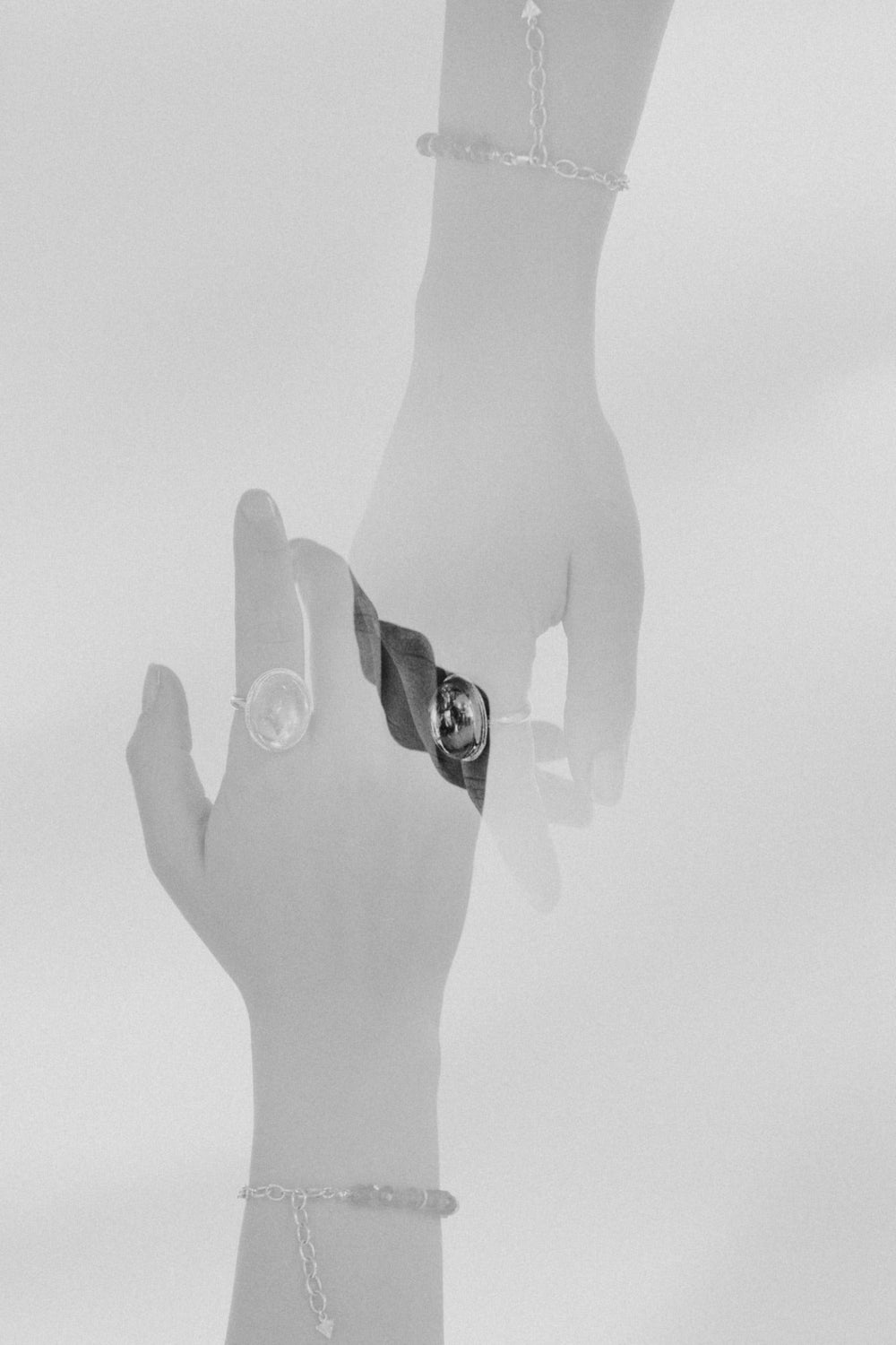 Two hands, overlapping each other in a double exposure, wear a ring by Emily Eliza Arlotte. The image is soft and greyscale.