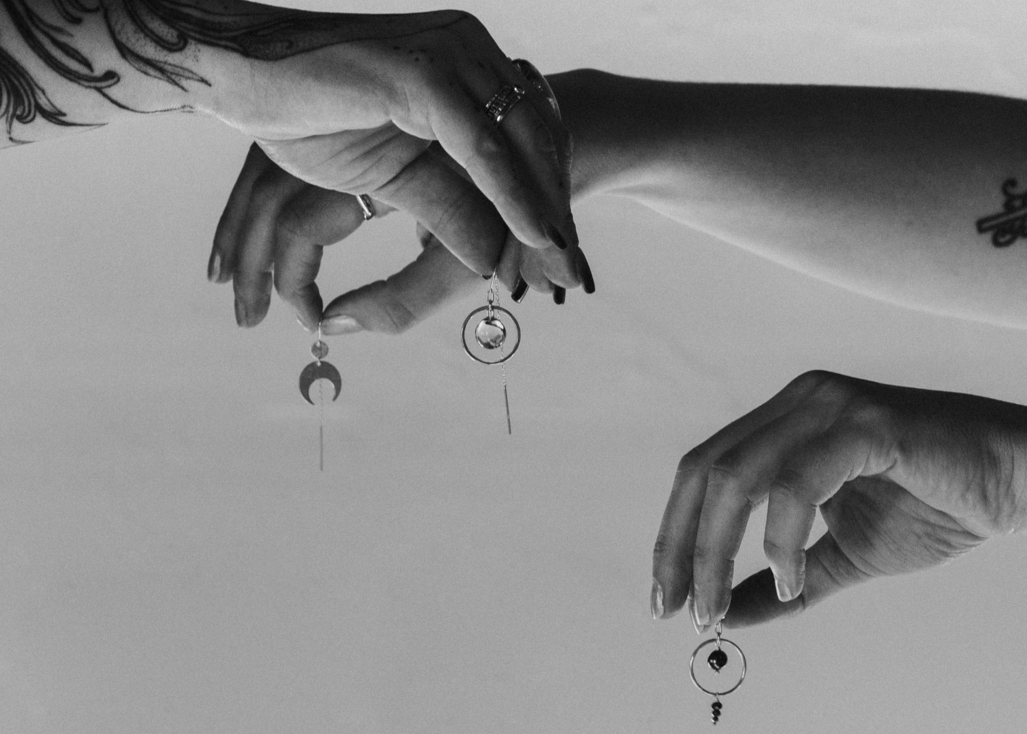 Black and white image of hands holding earrings by Emily Eliza Arlotte with a minimal background
