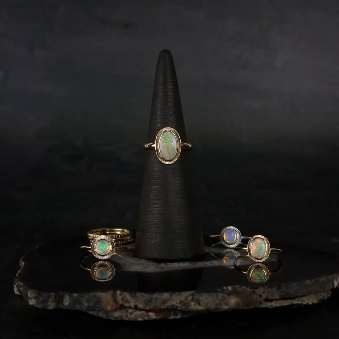Set of opal rings on a black stone surface with a dark background
