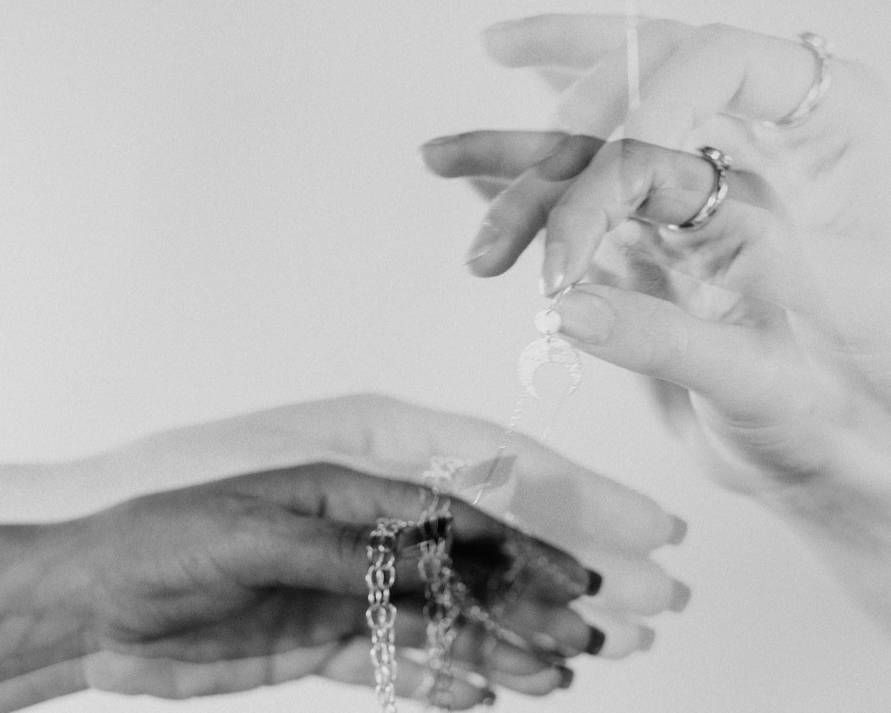The hands of Emily Eliza come into the images frame holding pieces of jewellery. The image is in black and white and is double exposed.